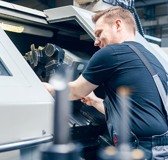 male technician operating machinery in workshop focused on precision work with metal components in industrial setting