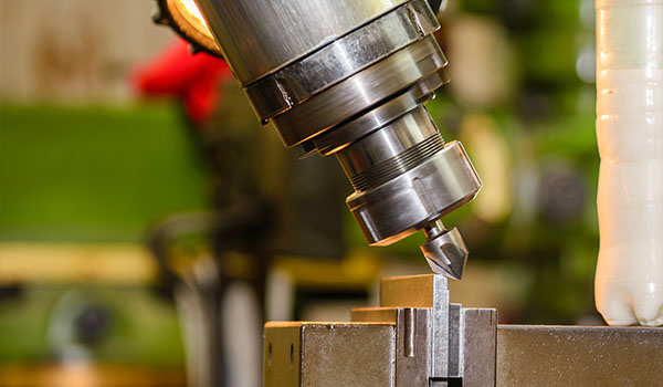 close up of a milling machine spindle with a cutting tool directed towards a workpiece highlighting precision machining techniques and tools. operations for creating exact 2 part components